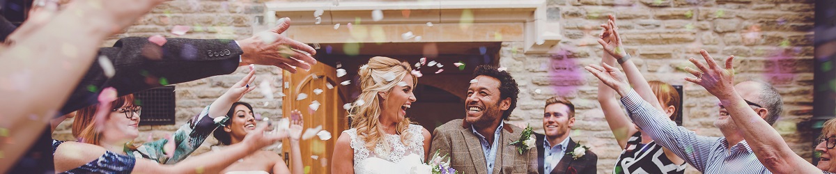 A bride and groom emerge from the Tudor Hall to confetti being thrown by attendees at their reception